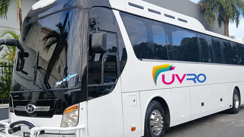Autobús UVRO blanco junto a una acera y palmeras